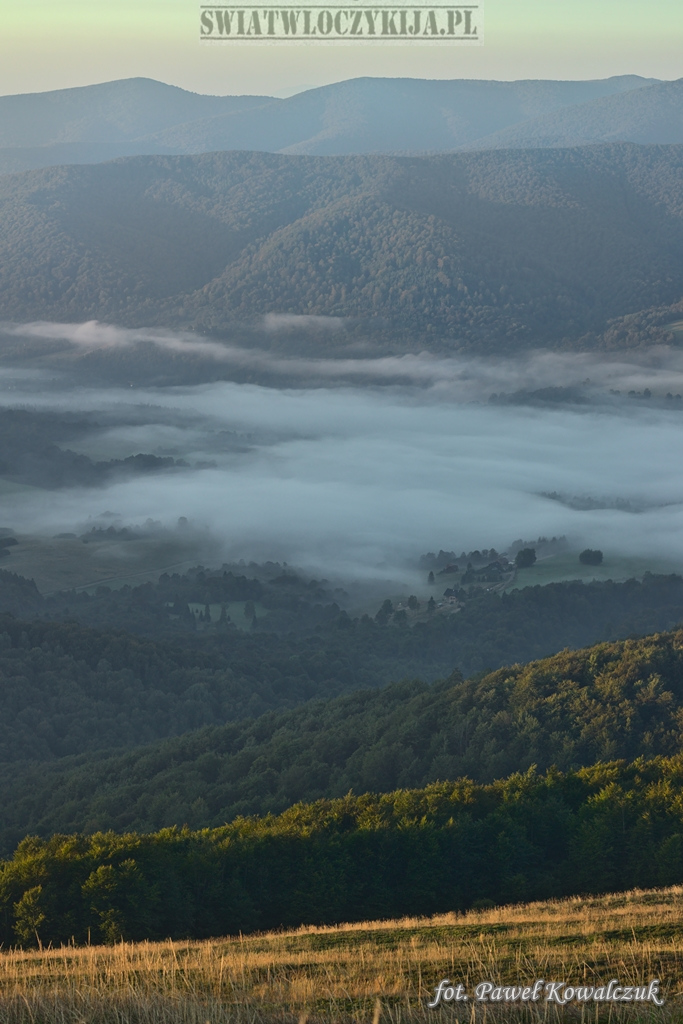 The valley in the Bieszczady Mountains is covered with dense fog and surrounded by undulating green mountains