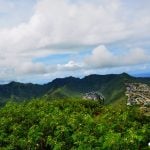 Zdjęcie przedstawia górzysta panoramę Oahu. Widoczne są zielone góry, zabudowania i dużo zieleni.